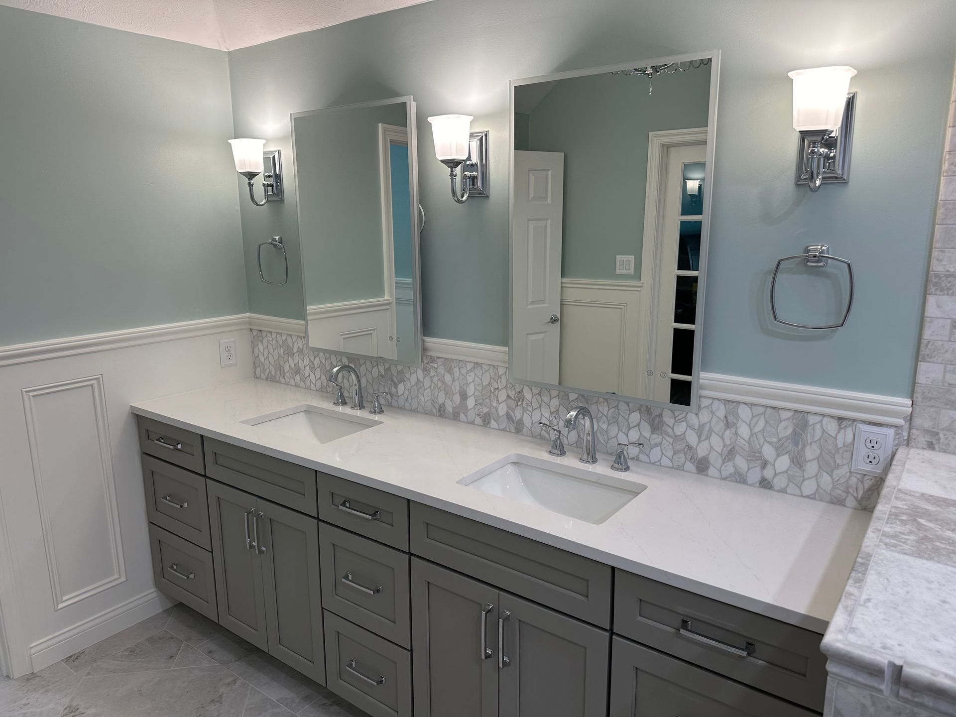 Spacious bathroom with double vanity, large mirror, wall sconces, and gray-green cabinets and walls