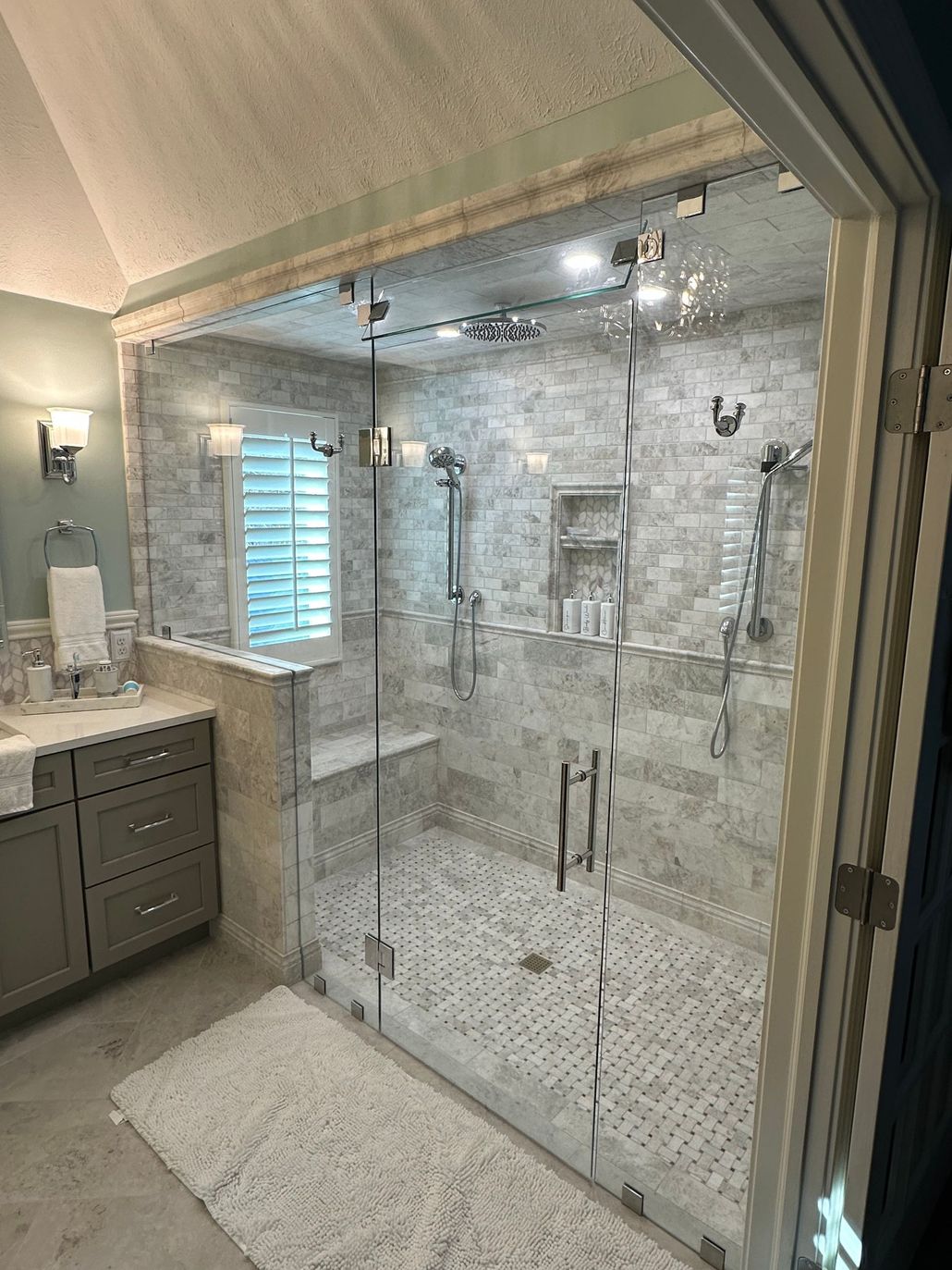 Luxury bathroom with a glass-enclosed marble shower, chrome fixtures, and a gray vanity beside it.