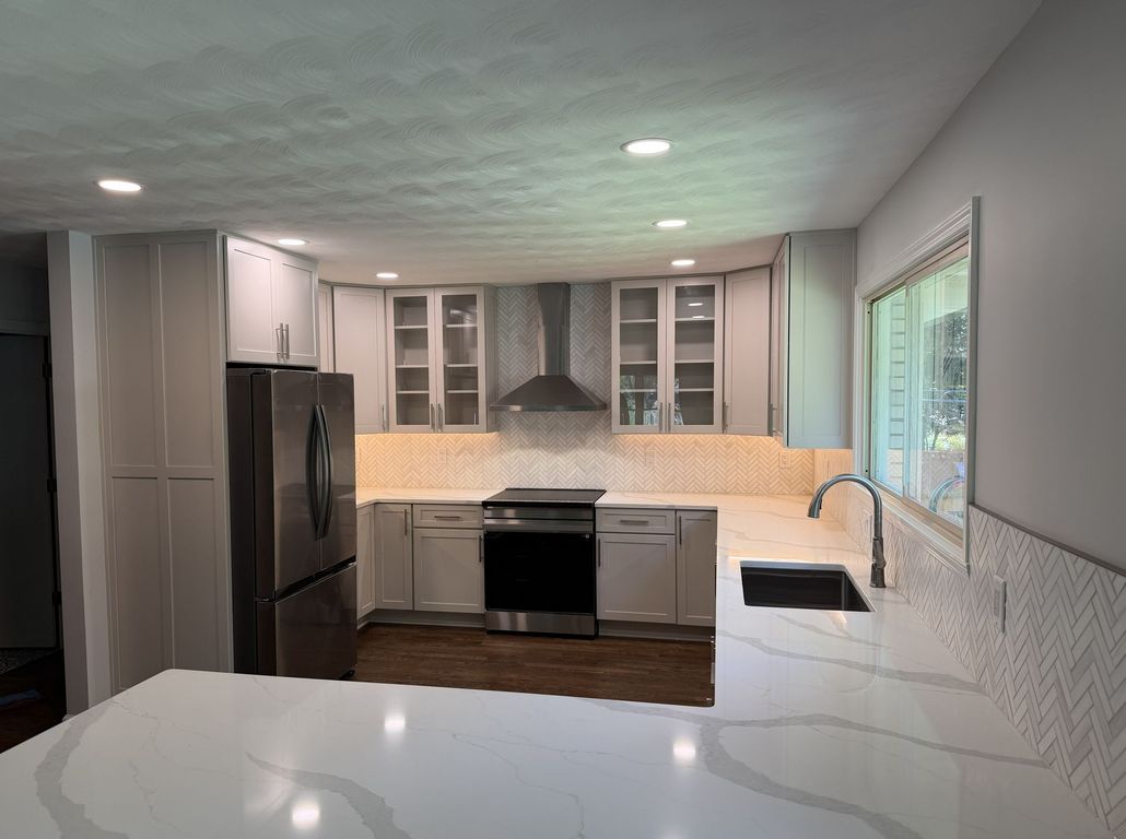 Bright modern kitchen with white island, stainless appliances, and gray cabinets.