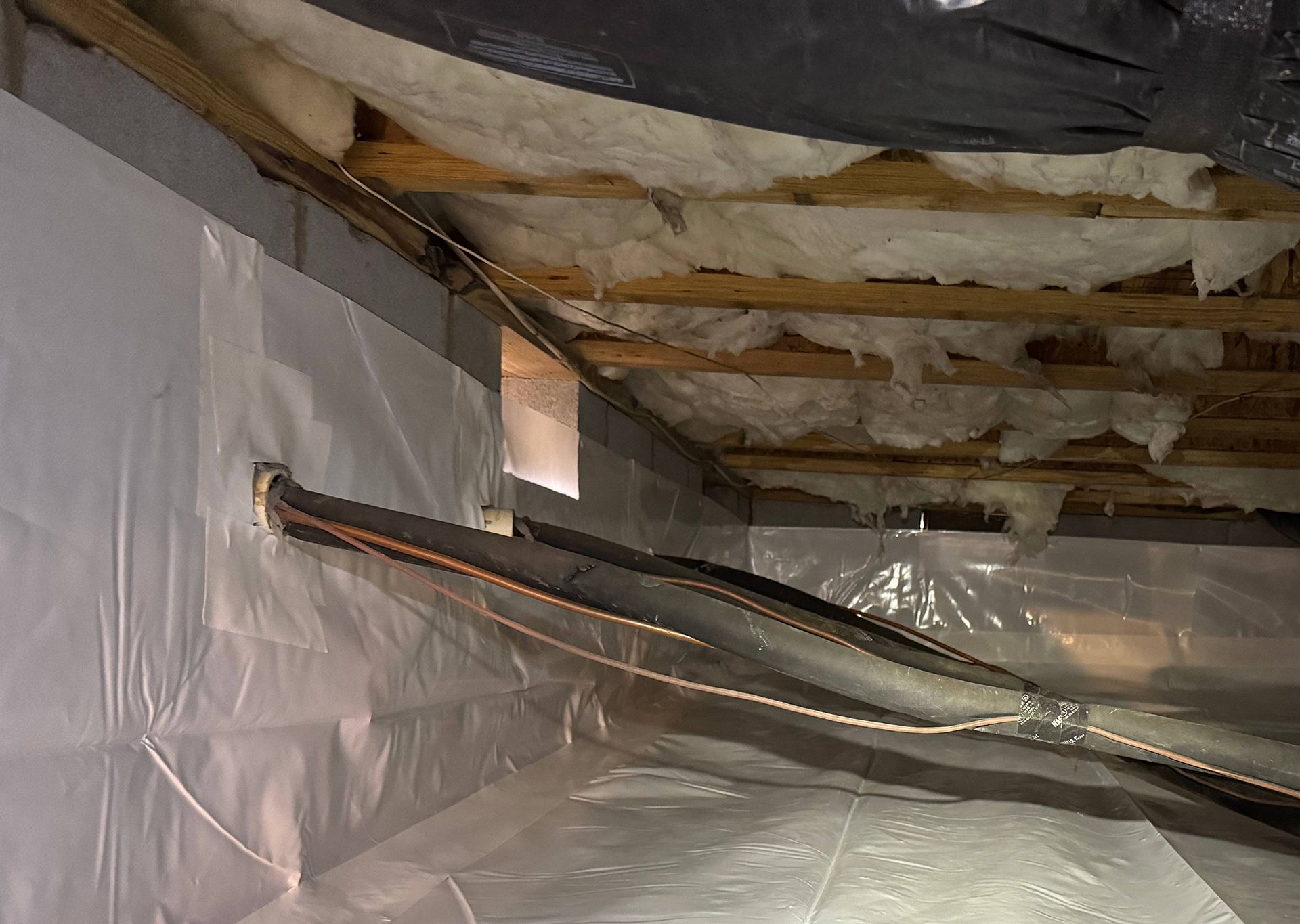 Crawl space with insulation and plastic sheeting on walls.