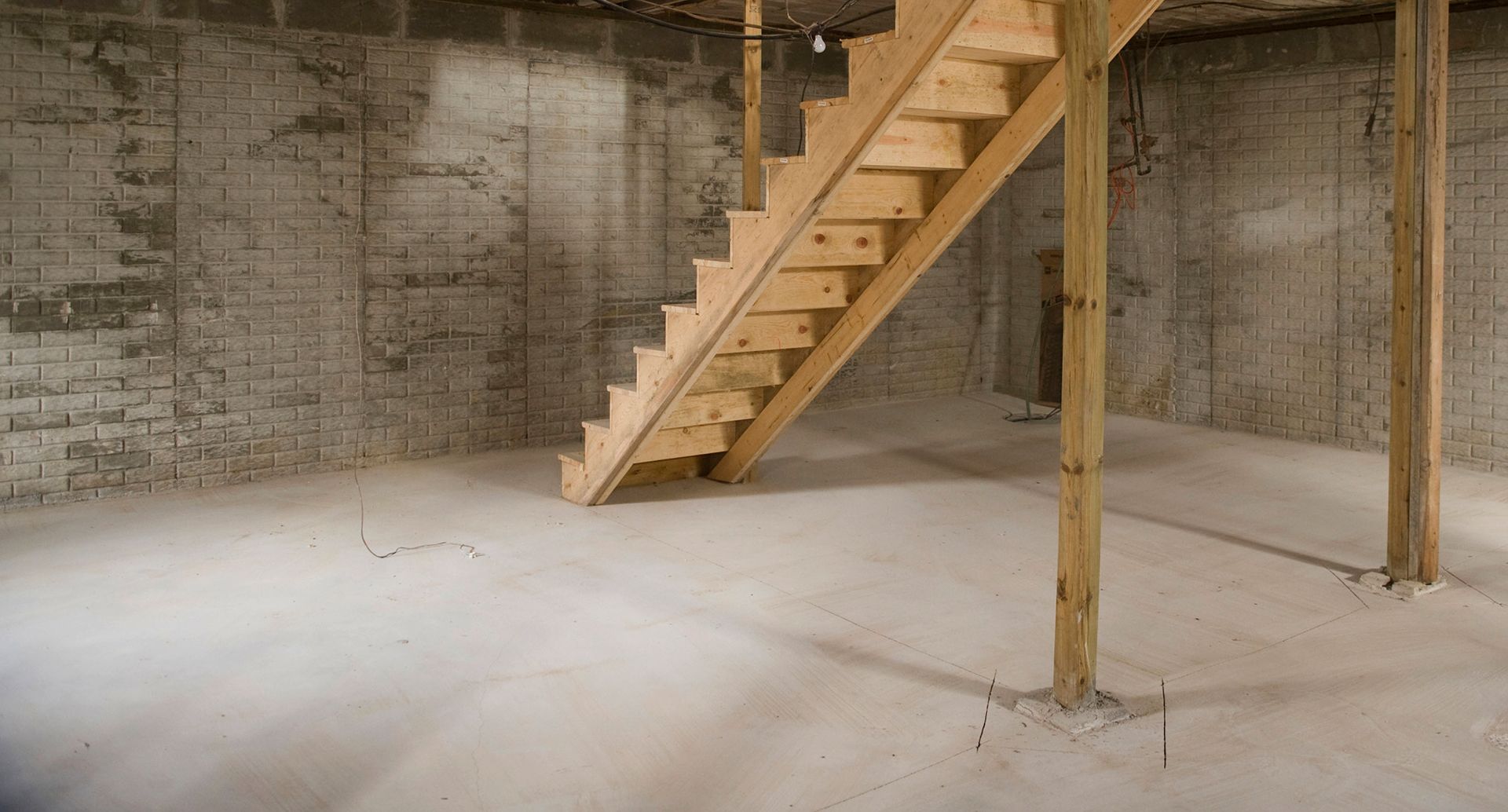 Bare concrete basement with wooden stairs and support posts.