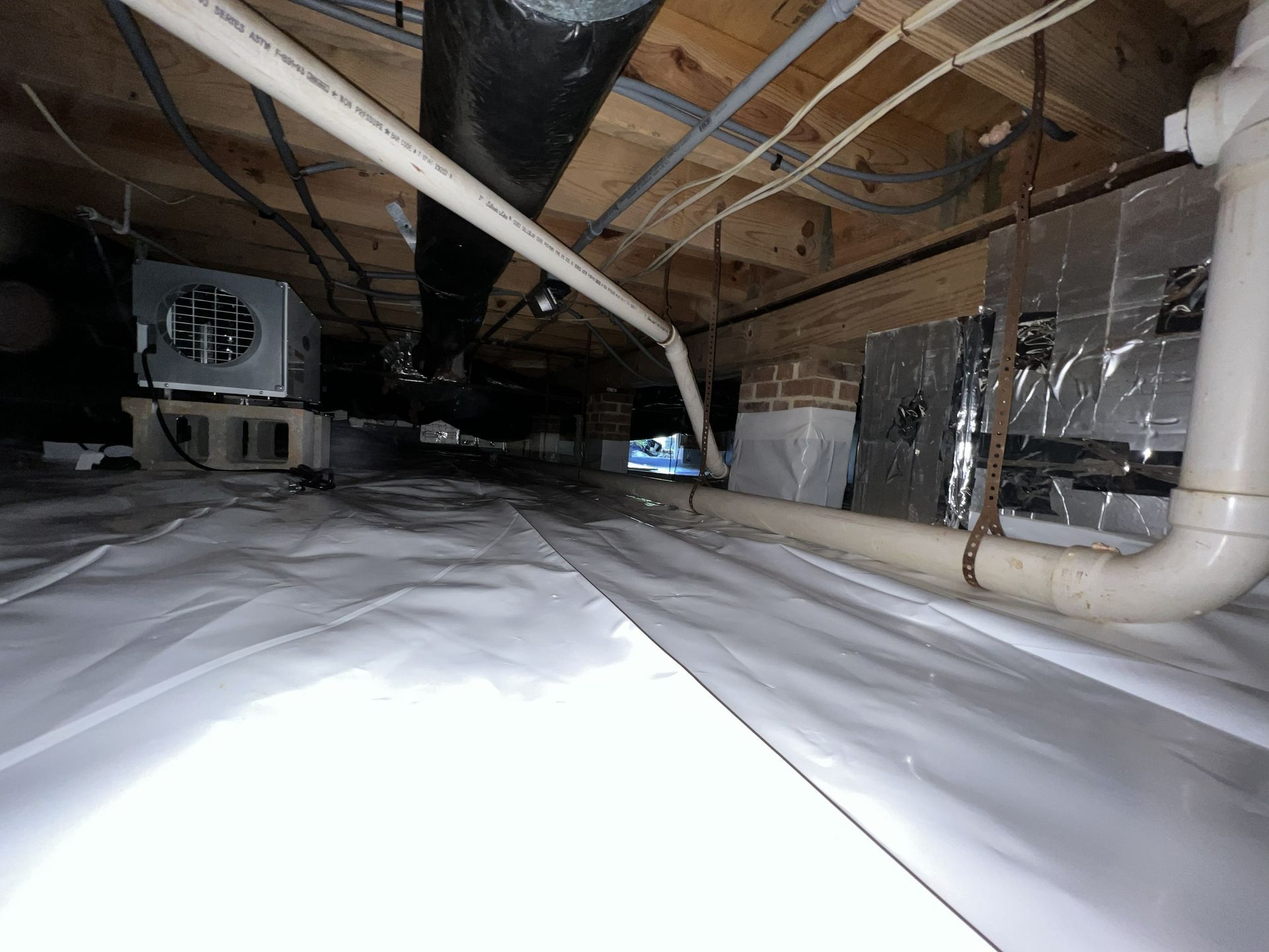 Crawl space with white vapor barrier, pipes, ductwork, and ventilation system.