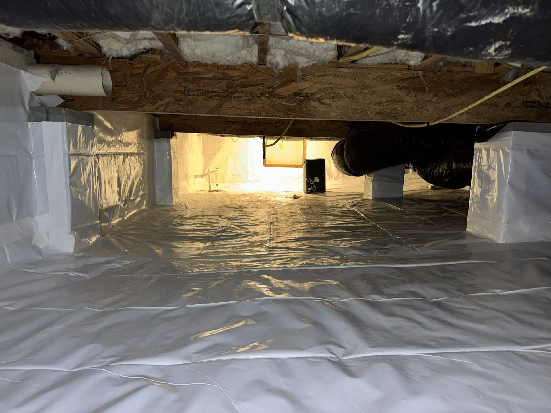 Crawl space with white plastic sheeting on the floor and walls, visible wooden beams and supports.
