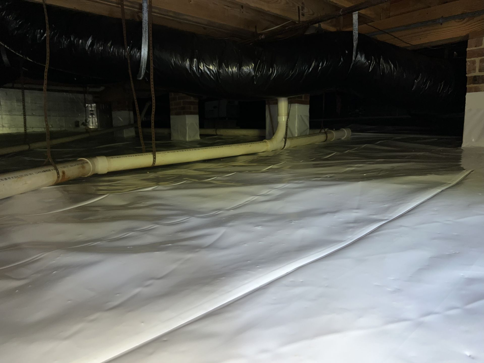 A crawl space covered in white plastic sheeting. Pipes and ductwork are visible.