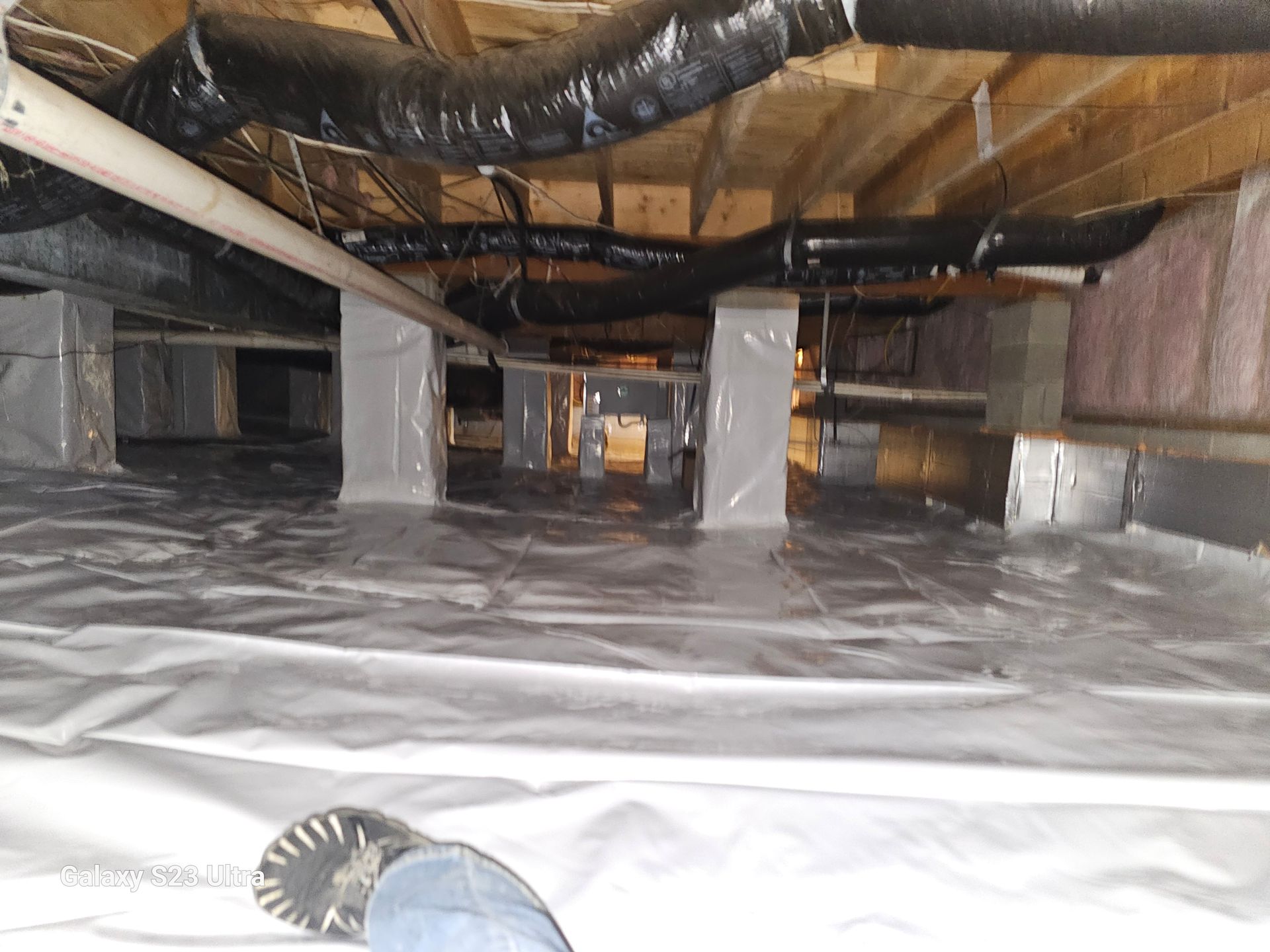 Crawlspace with vapor barrier on floor, insulation, and ductwork visible. White wrapped support posts.