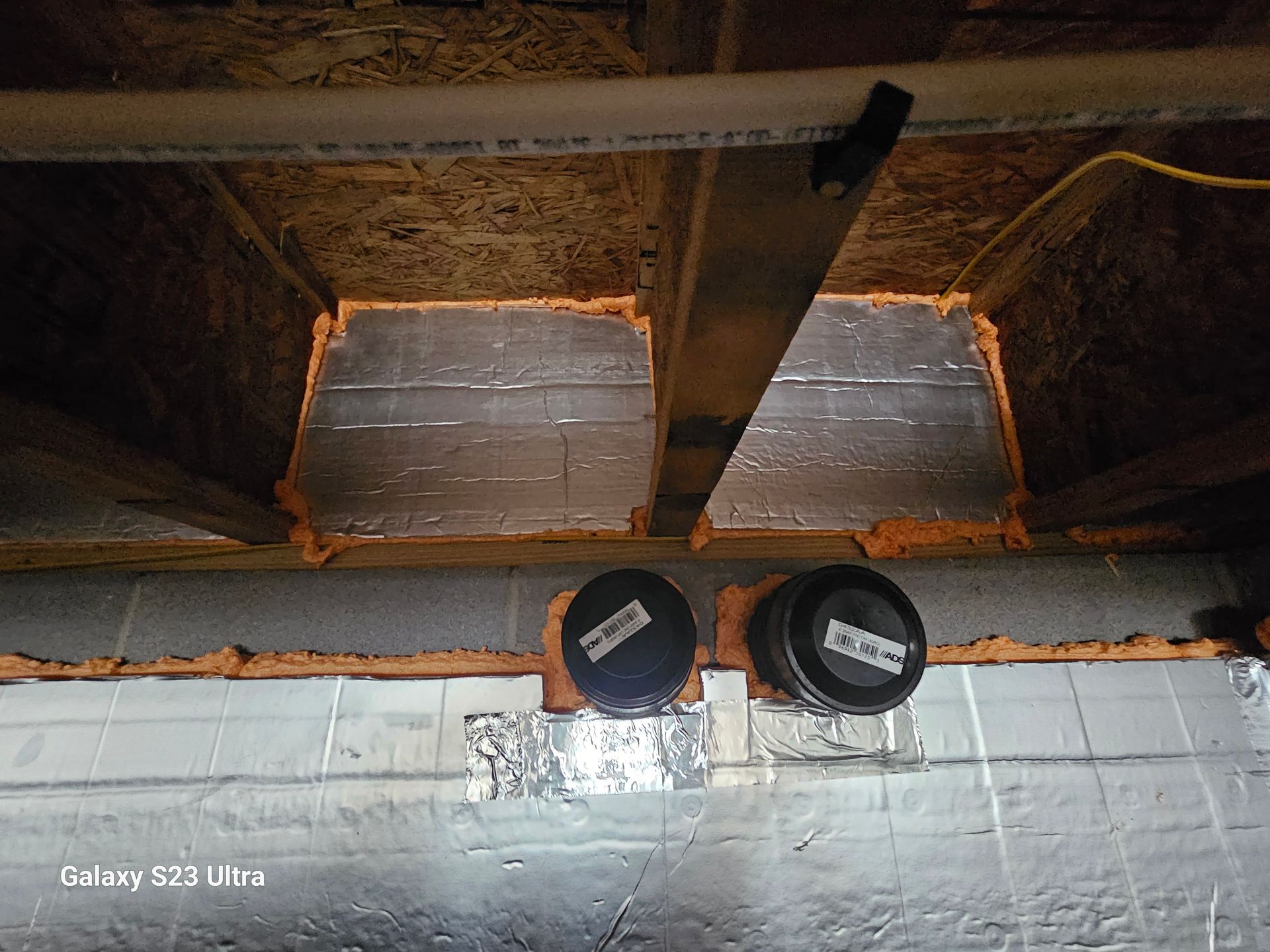 Two circular HVAC vents installed in a basement wall. Insulation is visible between the floor joists.