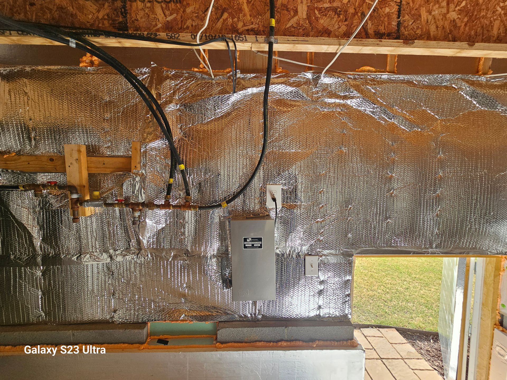 Electrical panel and wiring on a wall with insulation and an open window to the outdoors.