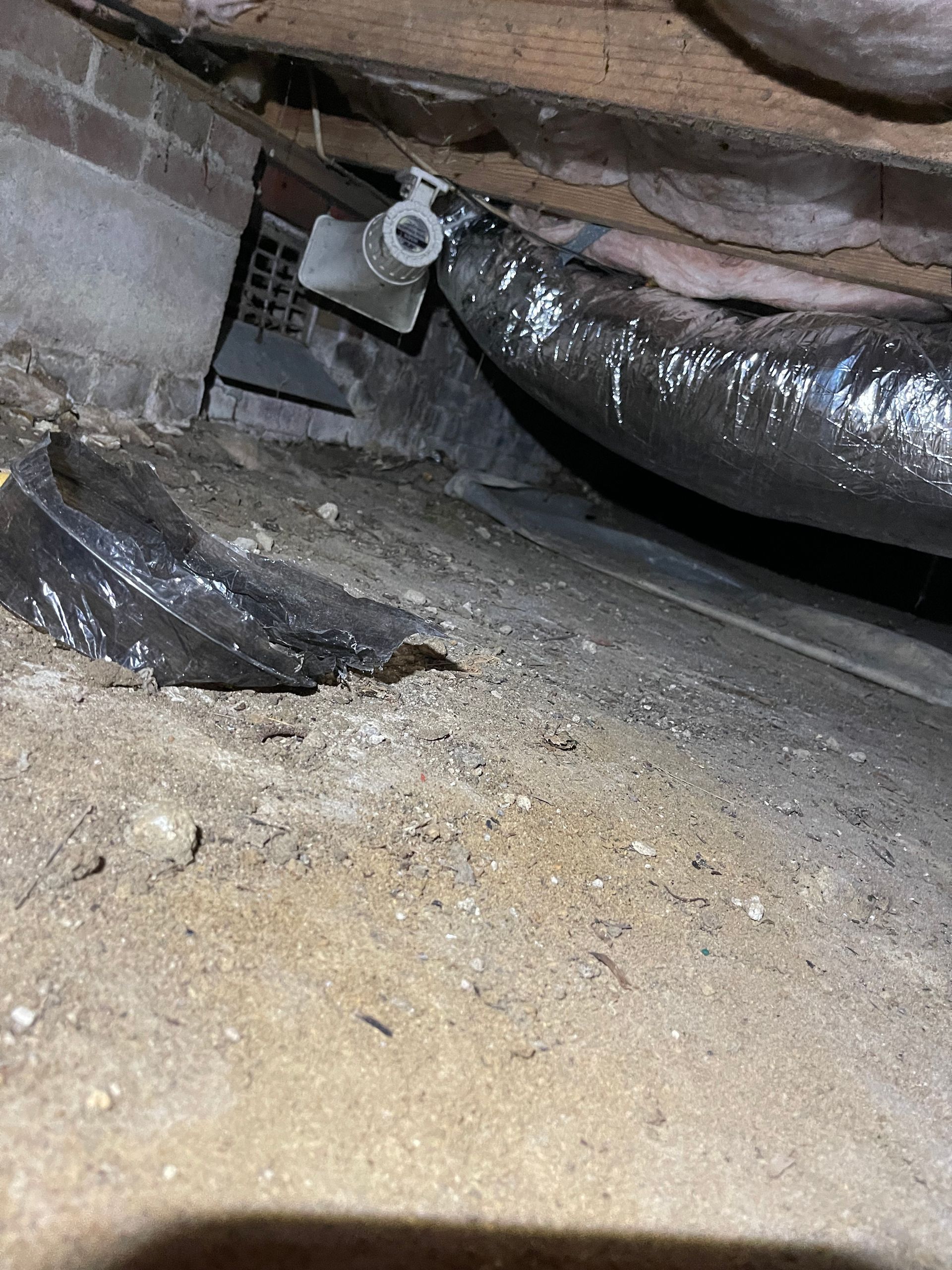 Underneath a structure: a dark, dusty crawl space with ventilation and ductwork.