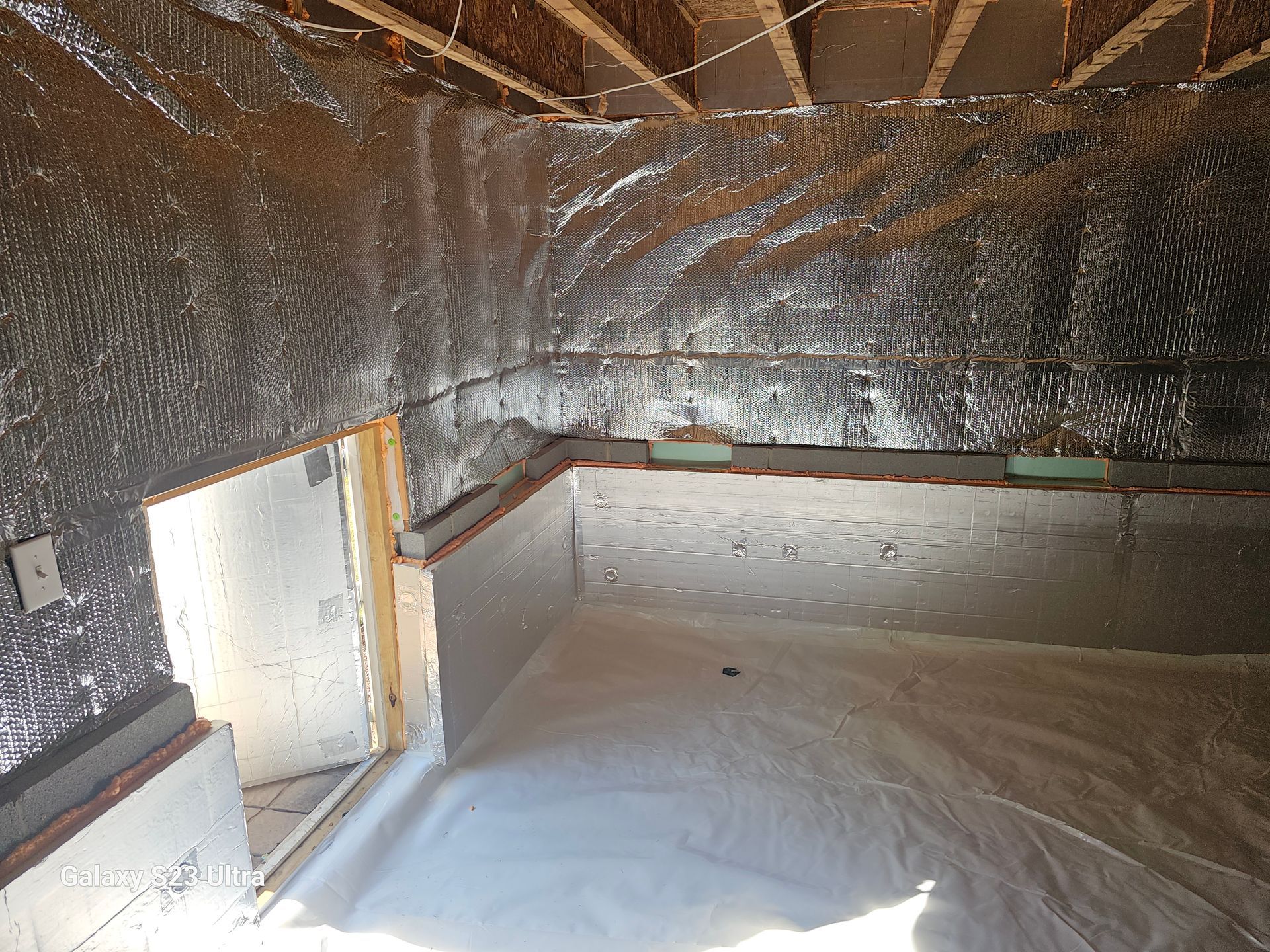 Crawl space with shiny, insulated walls and a white vapor barrier on the floor.