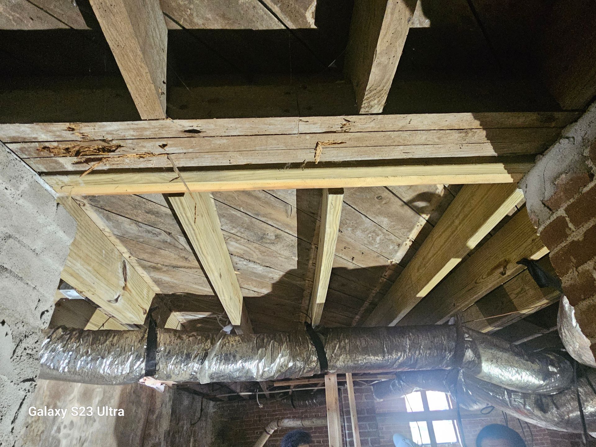 Wooden ceiling with exposed beams, brick and concrete walls, and ductwork.