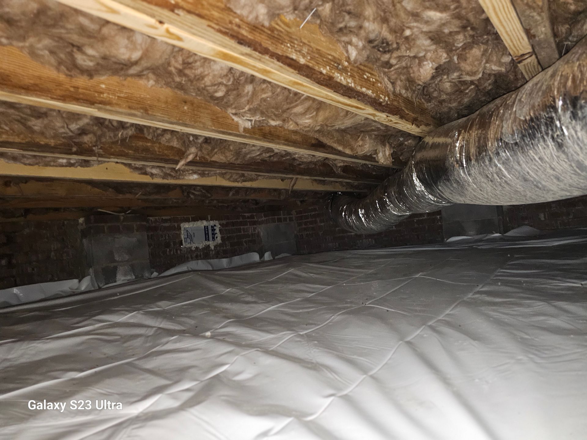Crawlspace with insulation, ductwork, vapor barrier, and mold on wood.