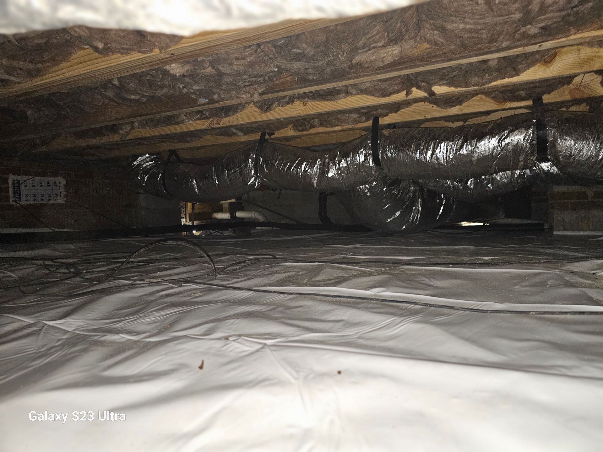 Crawlspace with silver vapor barrier, insulated ductwork, and exposed joists.