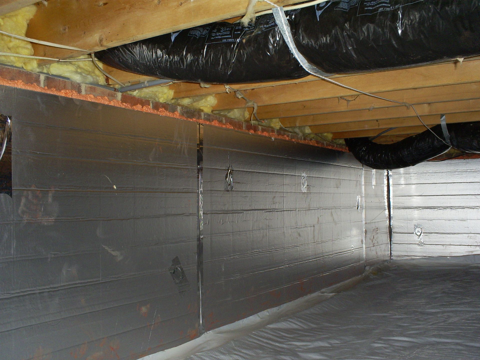 Crawlspace with reflective insulation on walls and floor, ductwork, and exposed wooden beams.