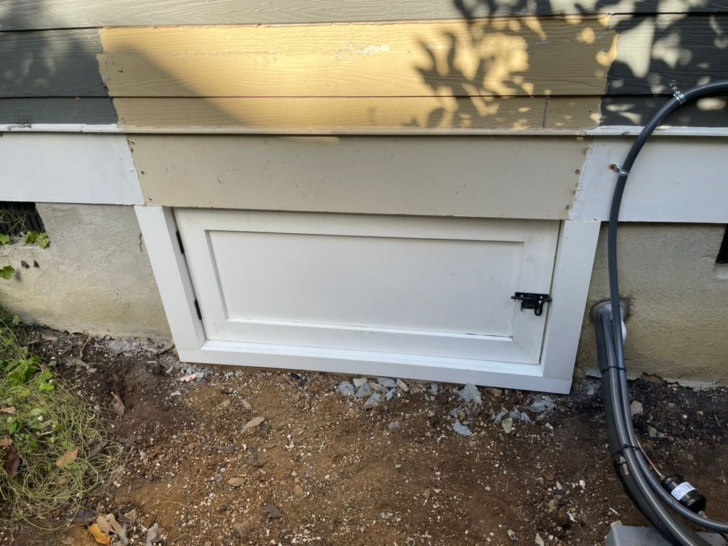 White door on a house foundation; dirt in front, siding above.