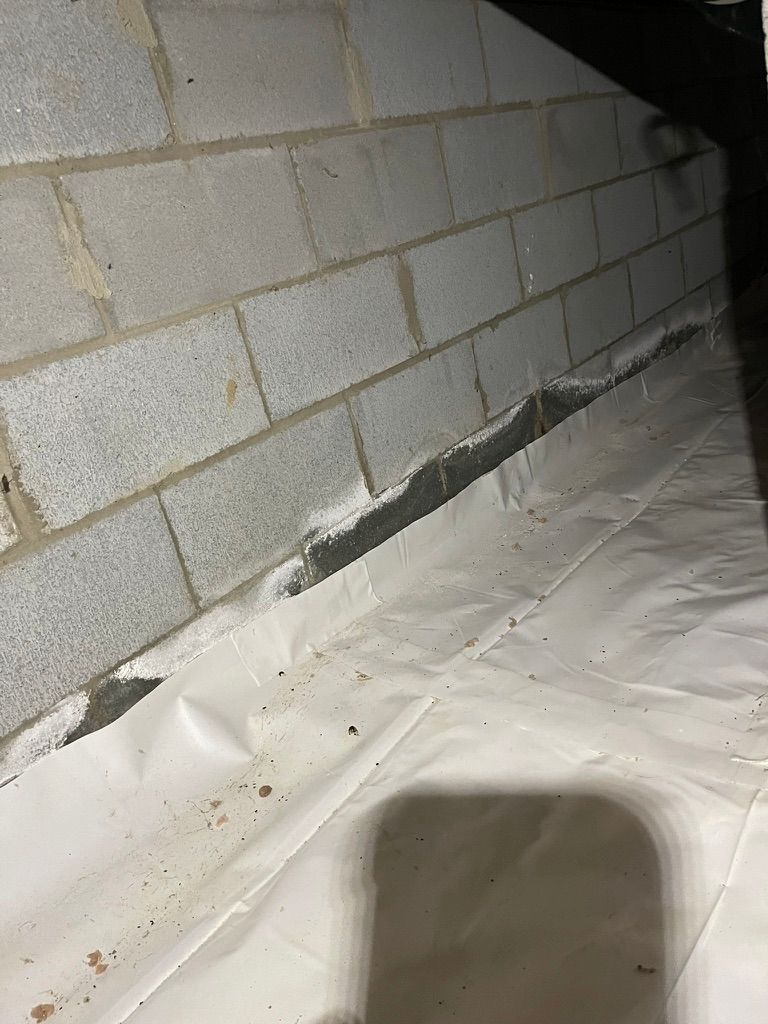 White plastic sheeting on a crawlspace floor against a cinder block wall.
