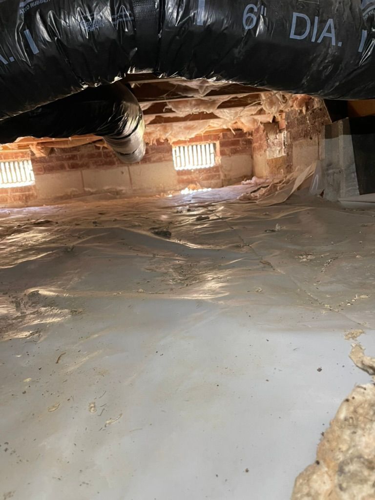 Crawl space under a building. Brick foundation with vents, a gray concrete floor, and black ductwork.