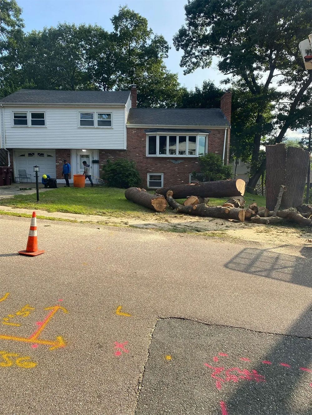 Damaged brick house and driveway with an open garage, scattered debris, and a traffic cone in front yard
