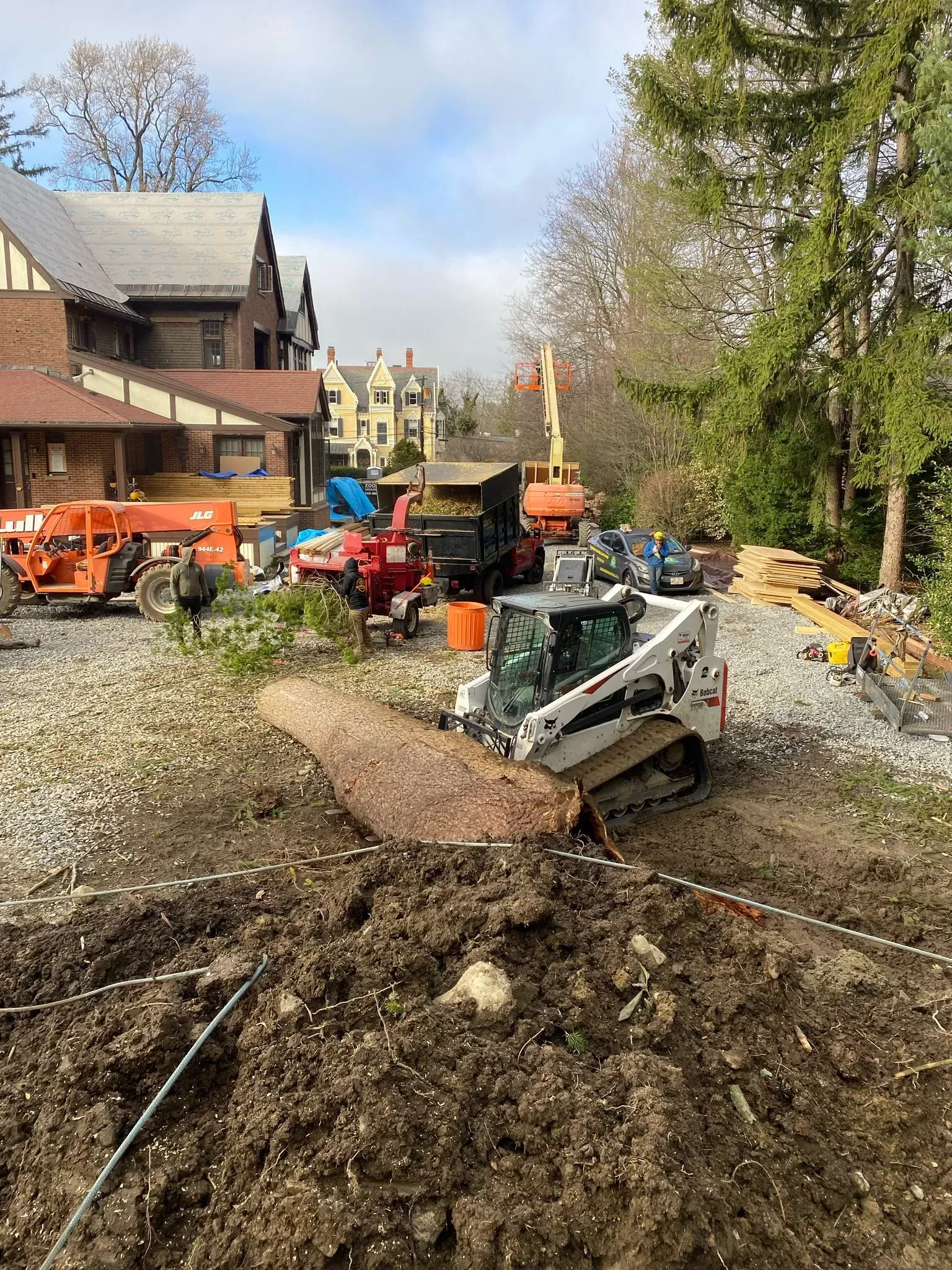Construction site with excavator and orange equipment beside a house, dirt and debris in the foreground.