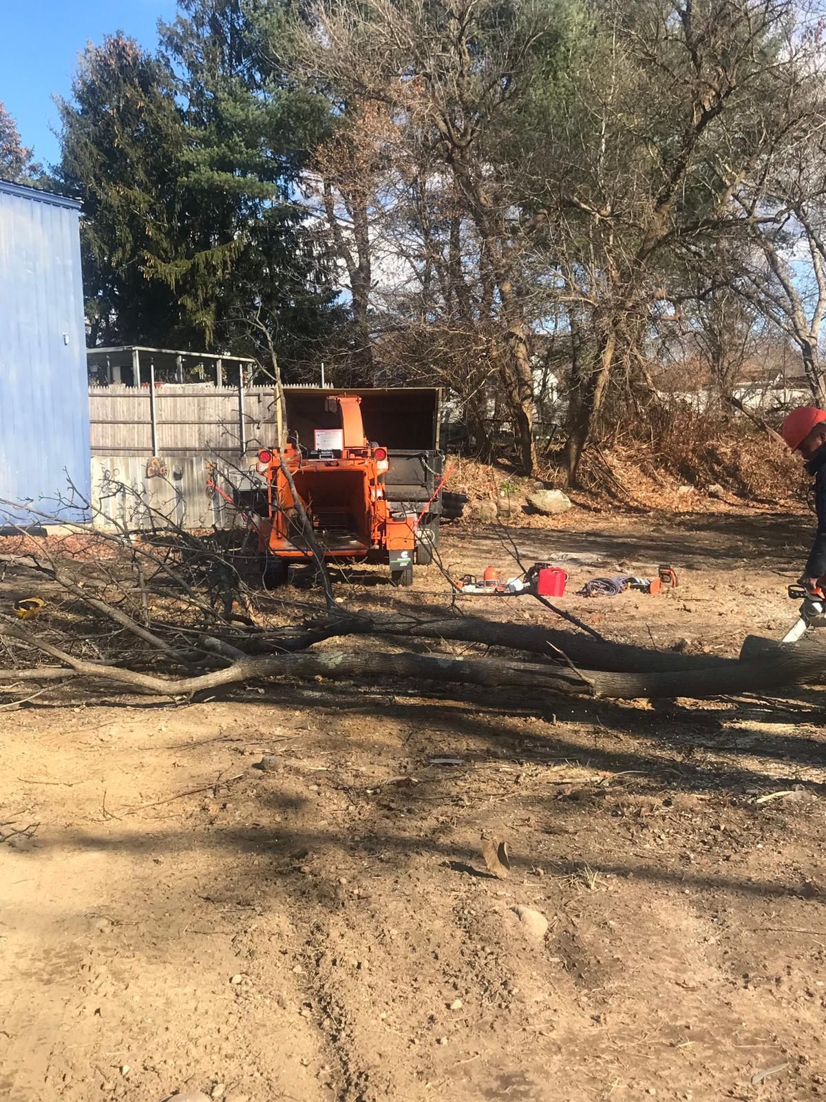 Orange tractor in a dusty yard beside a blue building, with trees and debris in the background