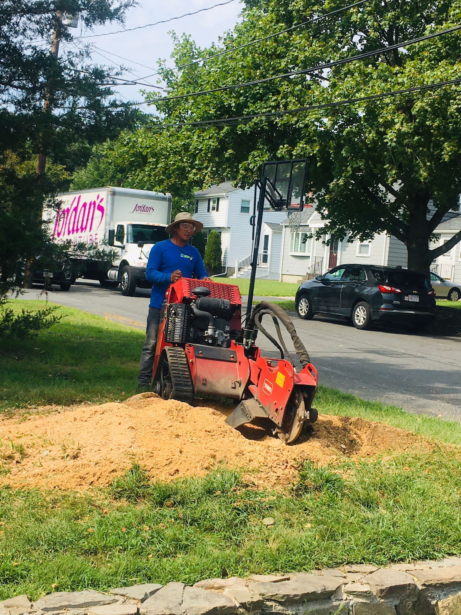 Worker using a red wood chipper on a grassy roadside with a pile of wood chips nearby