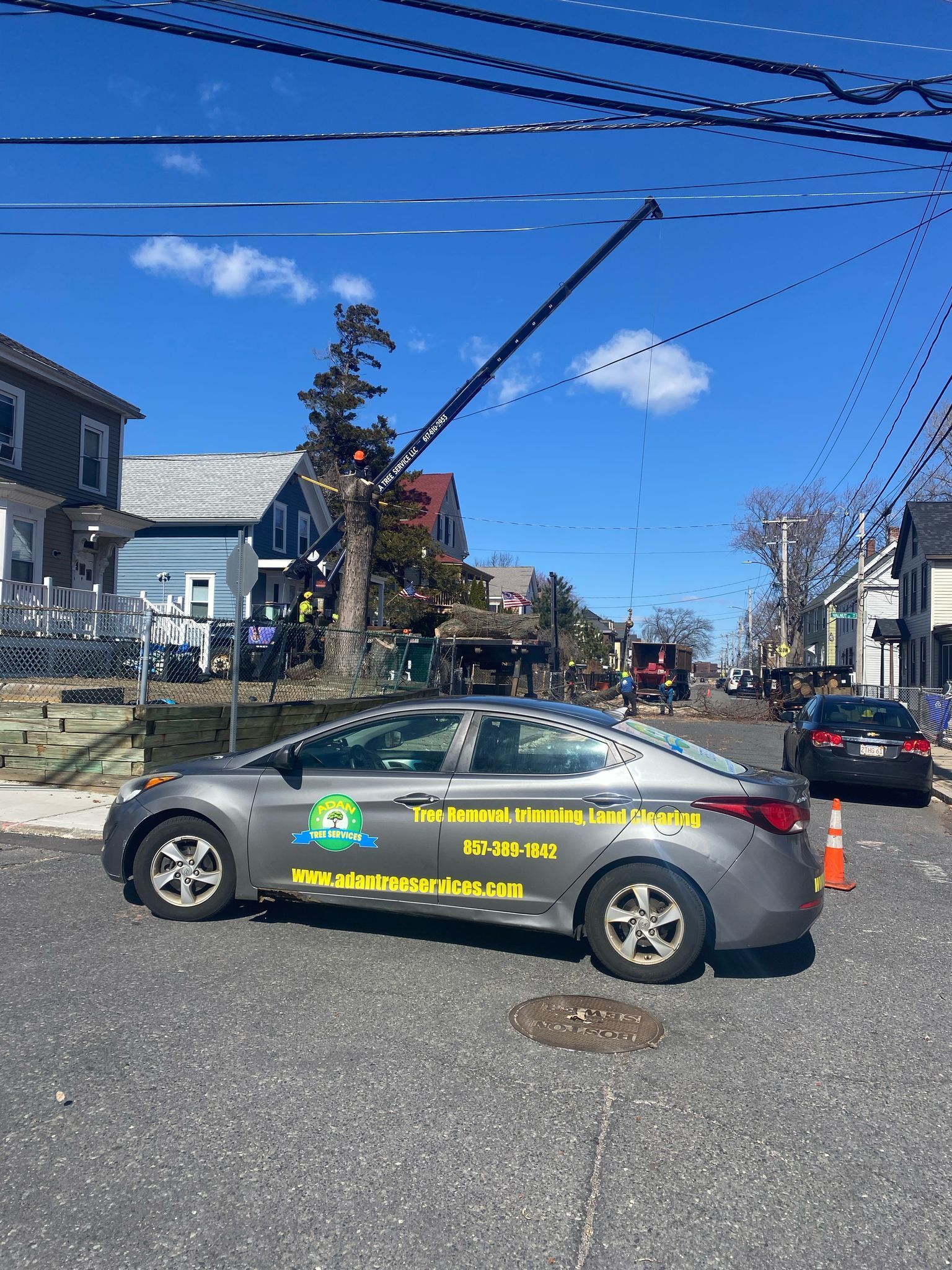 Gray sedan with yellow markings blocking a street, utility truck and orange cone in the background on a sunny day