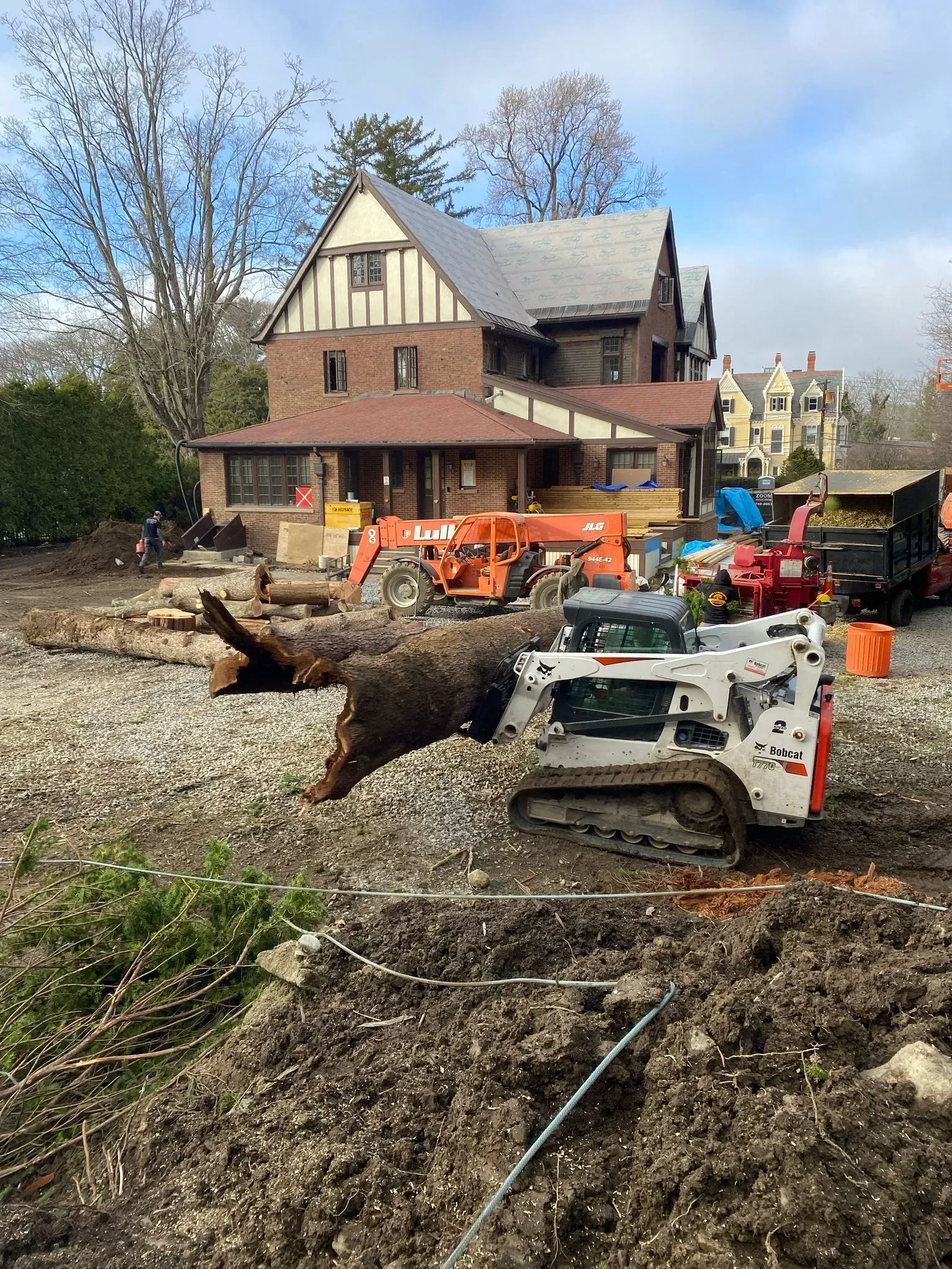 Construction equipment clearing a large fallen tree near a house in a yard