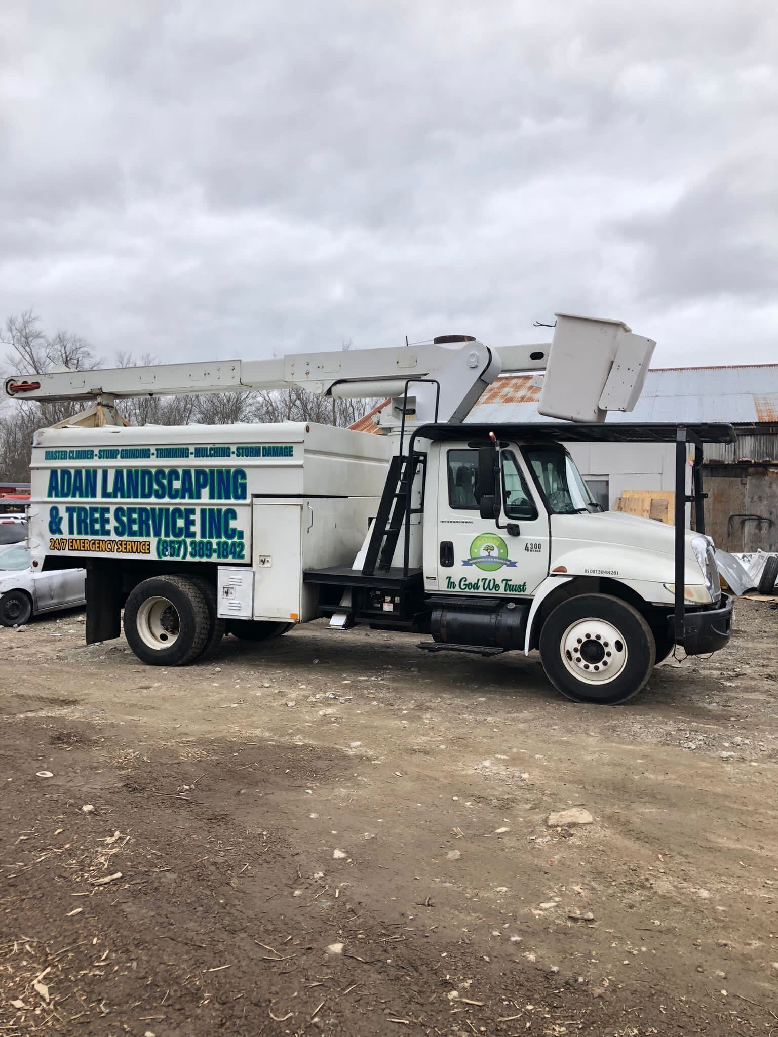 White utility truck with raised boom and large sign parked on a dirt lot under a cloudy sky.