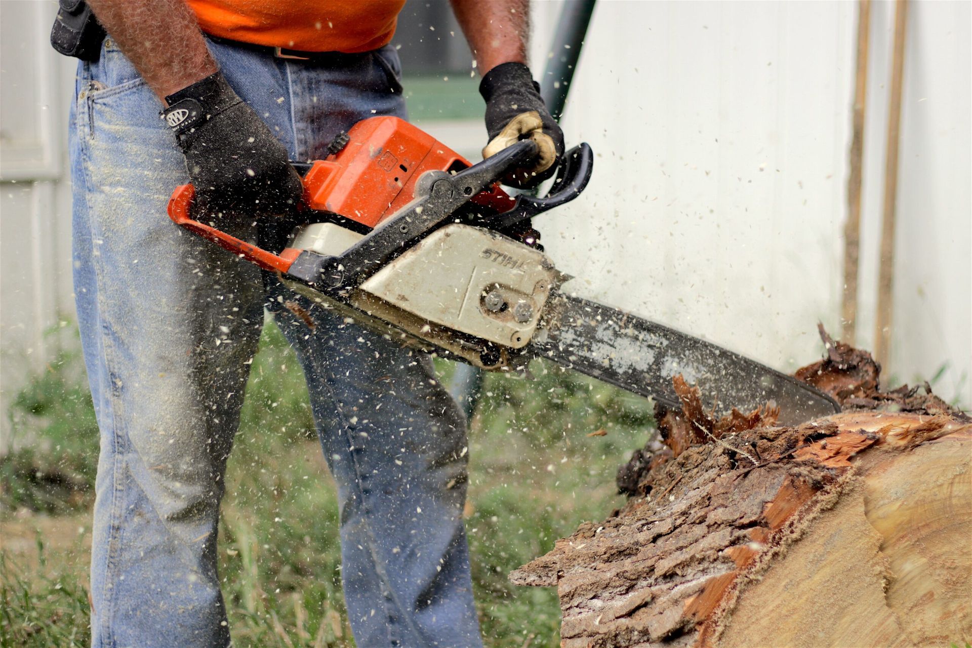 Worker cutting a log with a chainsaw, sawdust flying outdoors.