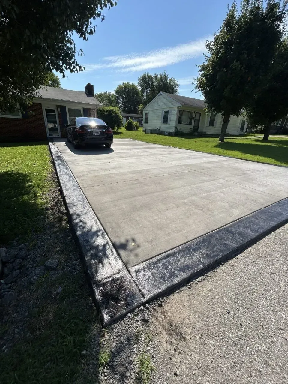Concrete driveway with black border, car parked in front of a house, sunny day.