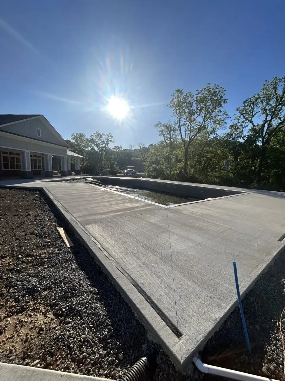 Newly poured concrete pool deck with surrounding landscape under a sunny sky.