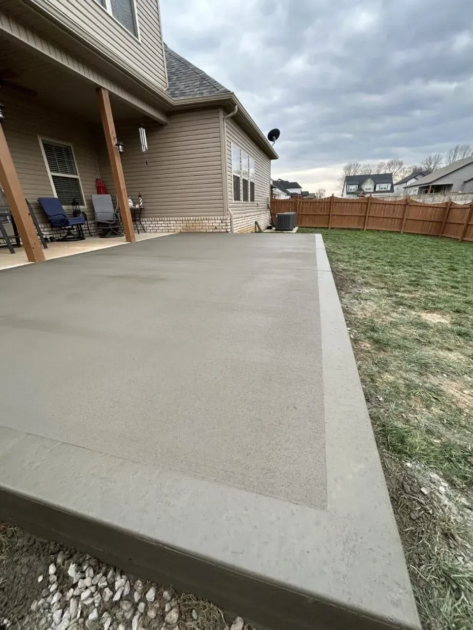 Newly poured concrete patio next to a house with a backyard fence.