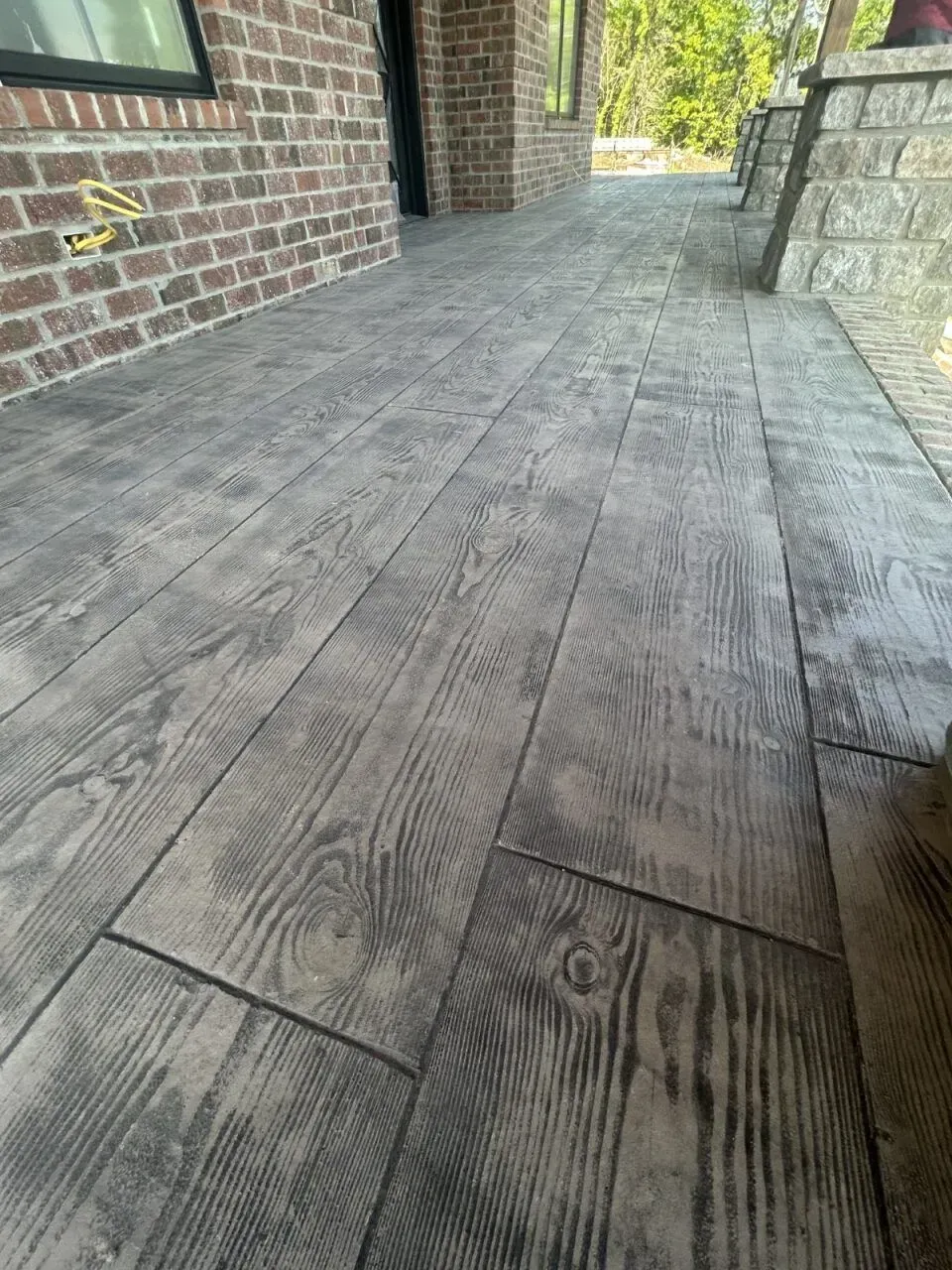 Wood-look stamped concrete patio, gray tones, next to a brick wall.