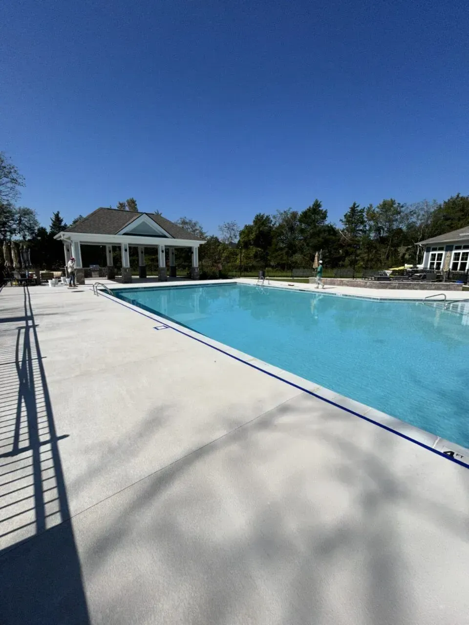 Swimming pool with white concrete deck, blue water, and a gazebo on a sunny day.