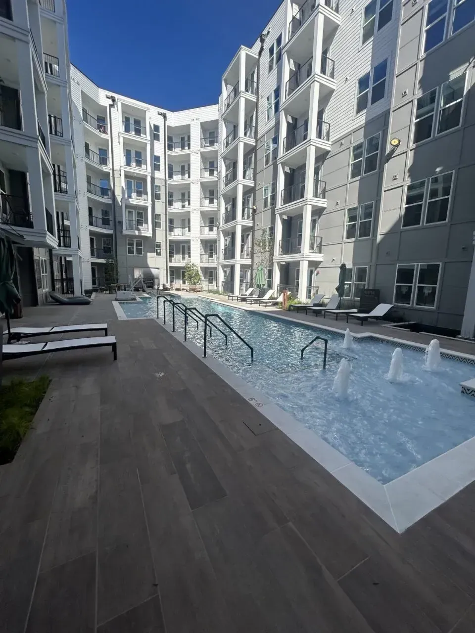 Swimming pool in courtyard of modern apartment complex. Buildings have balconies.