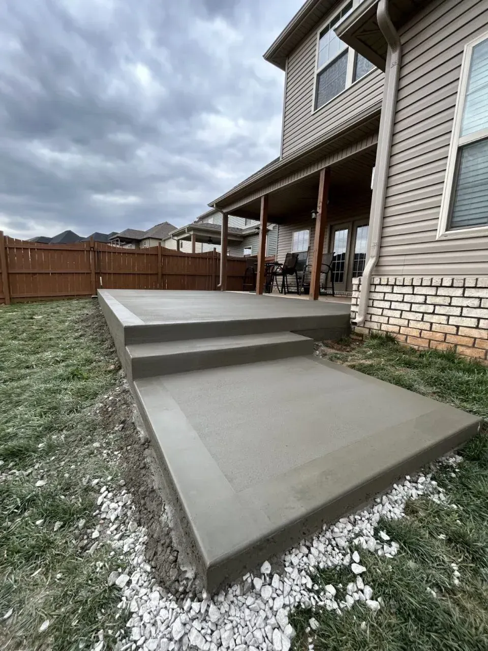 Newly poured concrete patio with steps next to a house with beige siding and a covered porch.