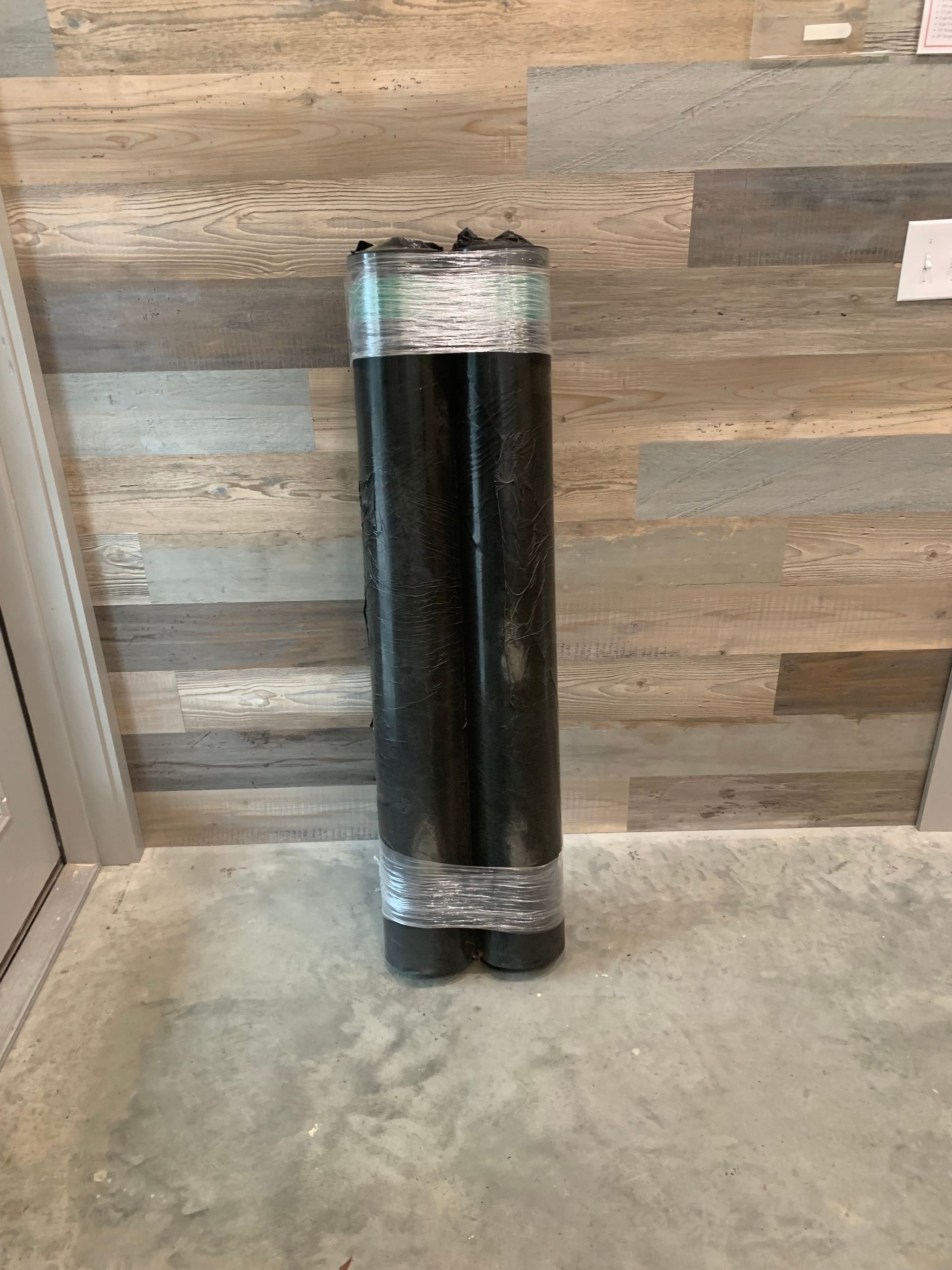 A roll of black duct tape is sitting on a concrete floor in front of a wooden wall.