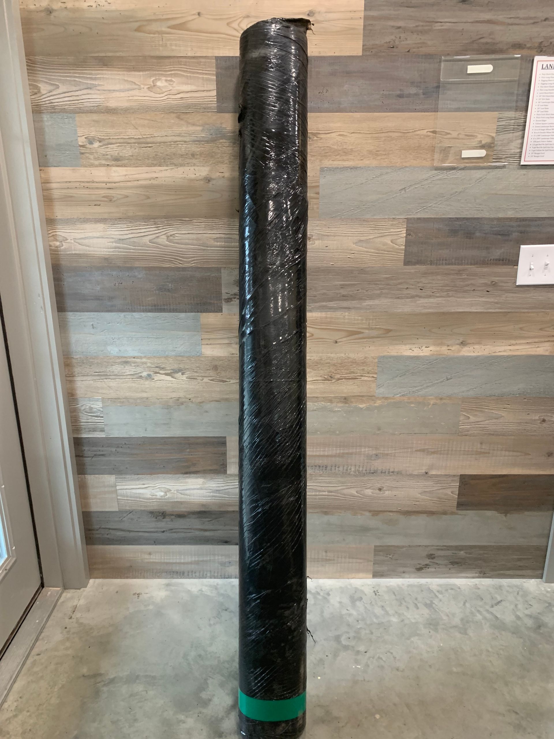A black pole is sitting in front of a wooden wall.