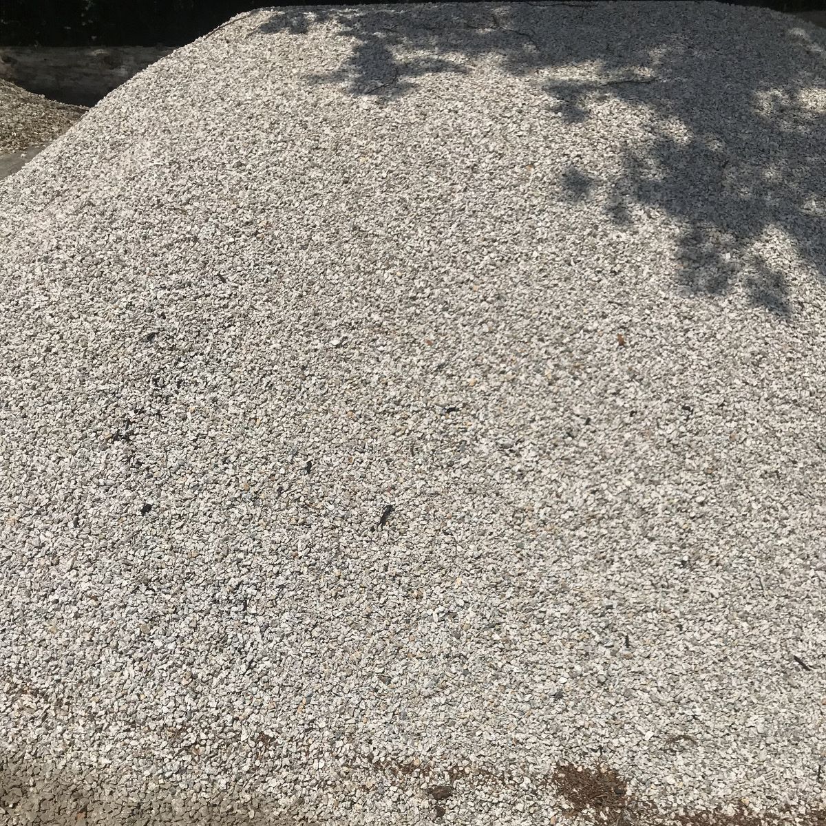 A pile of gravel is sitting on the ground next to a tree.