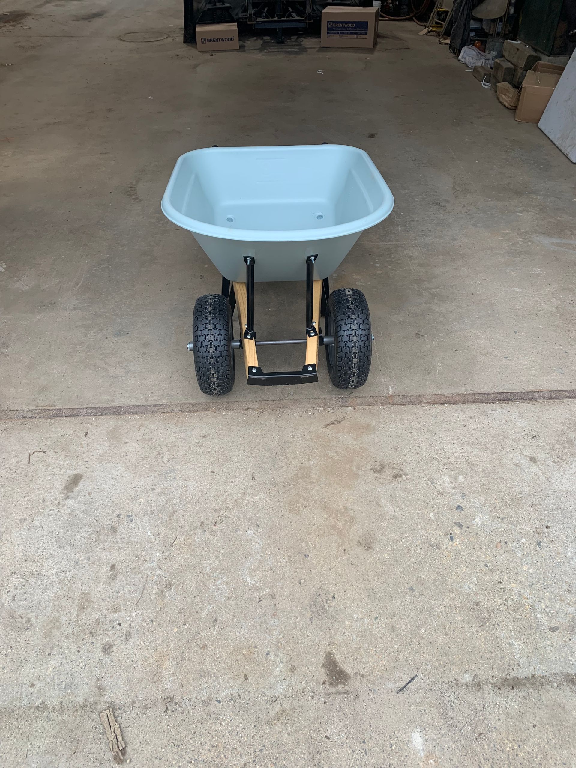 A small wheelbarrow is sitting on the ground in a garage.