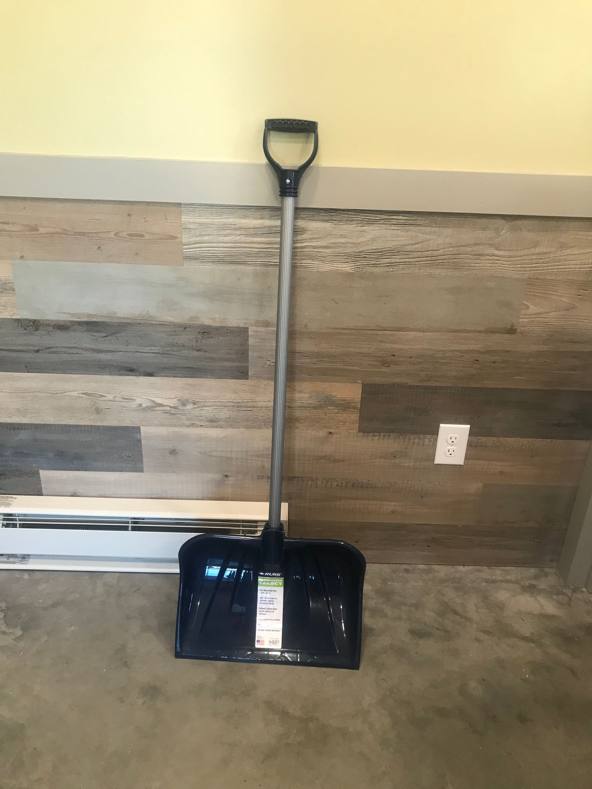 A snow shovel is sitting on a wooden floor next to a wall.
