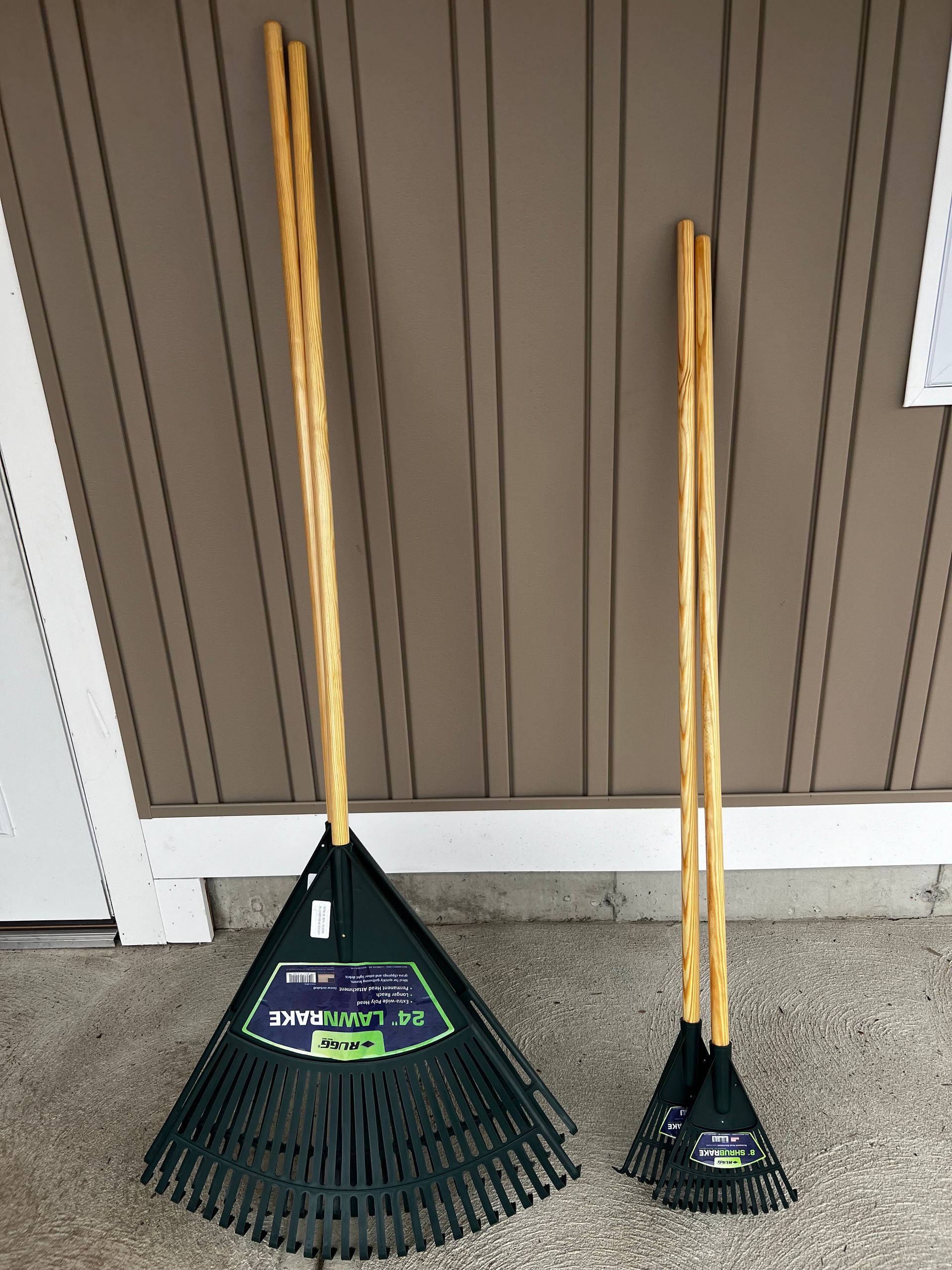 Two rakes with wooden handles are sitting next to each other on the ground.