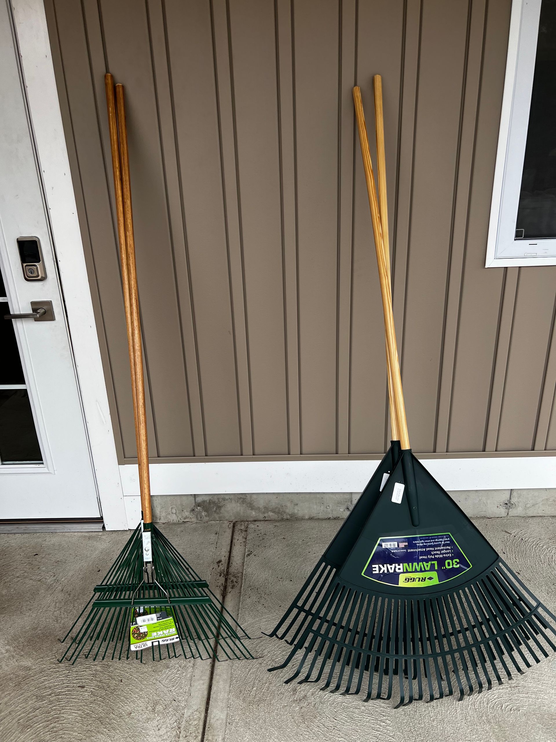 Two rakes with wooden handles are sitting on a sidewalk in front of a building.