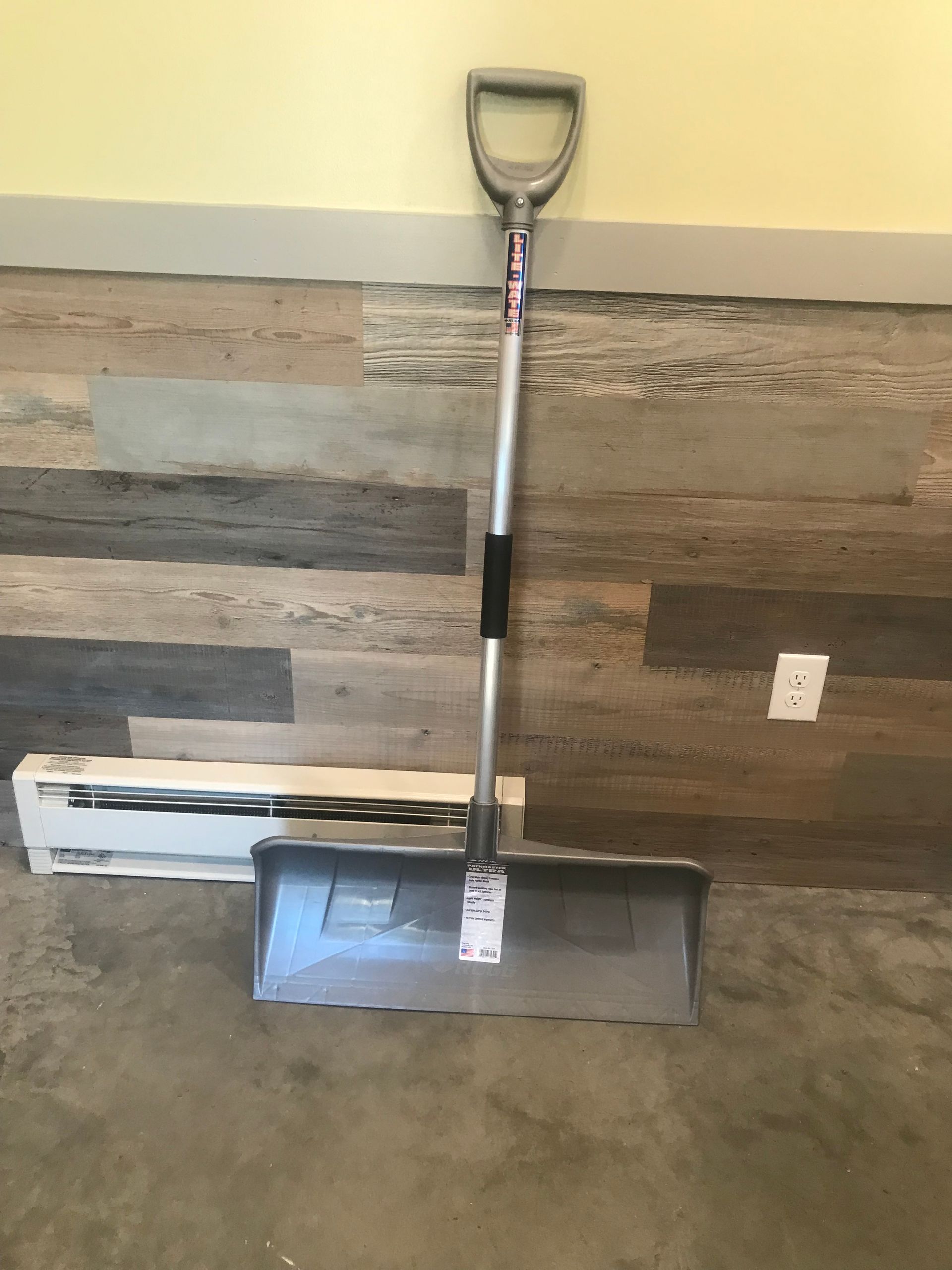 A snow shovel is sitting on a wooden floor.