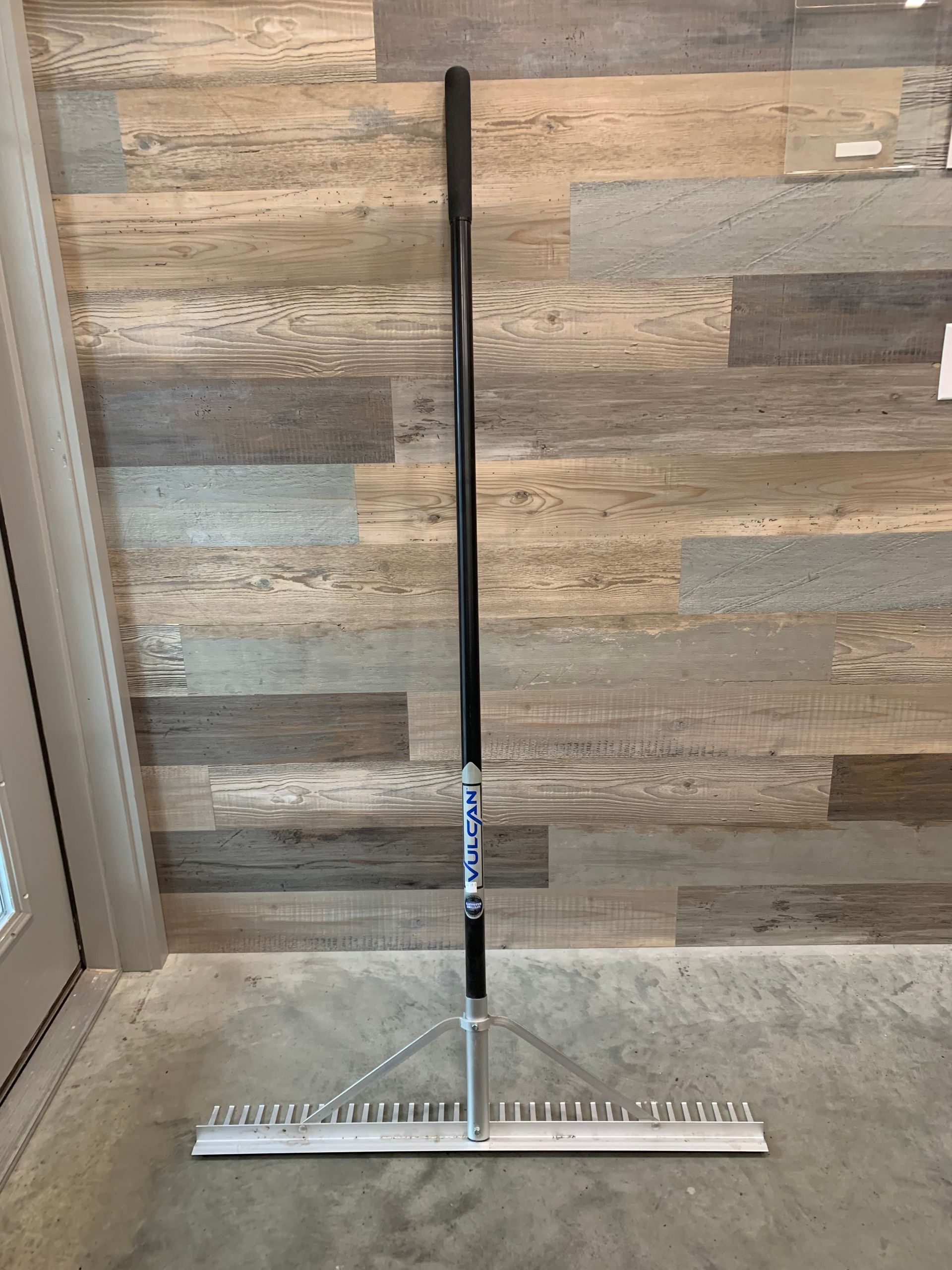 A rake is sitting on the floor in front of a wooden wall.