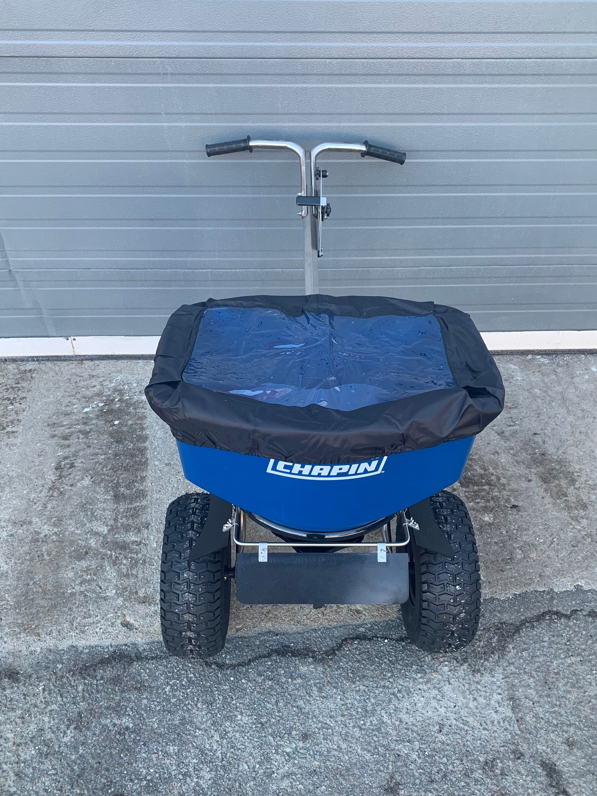 A blue spreader is parked in front of a garage door.