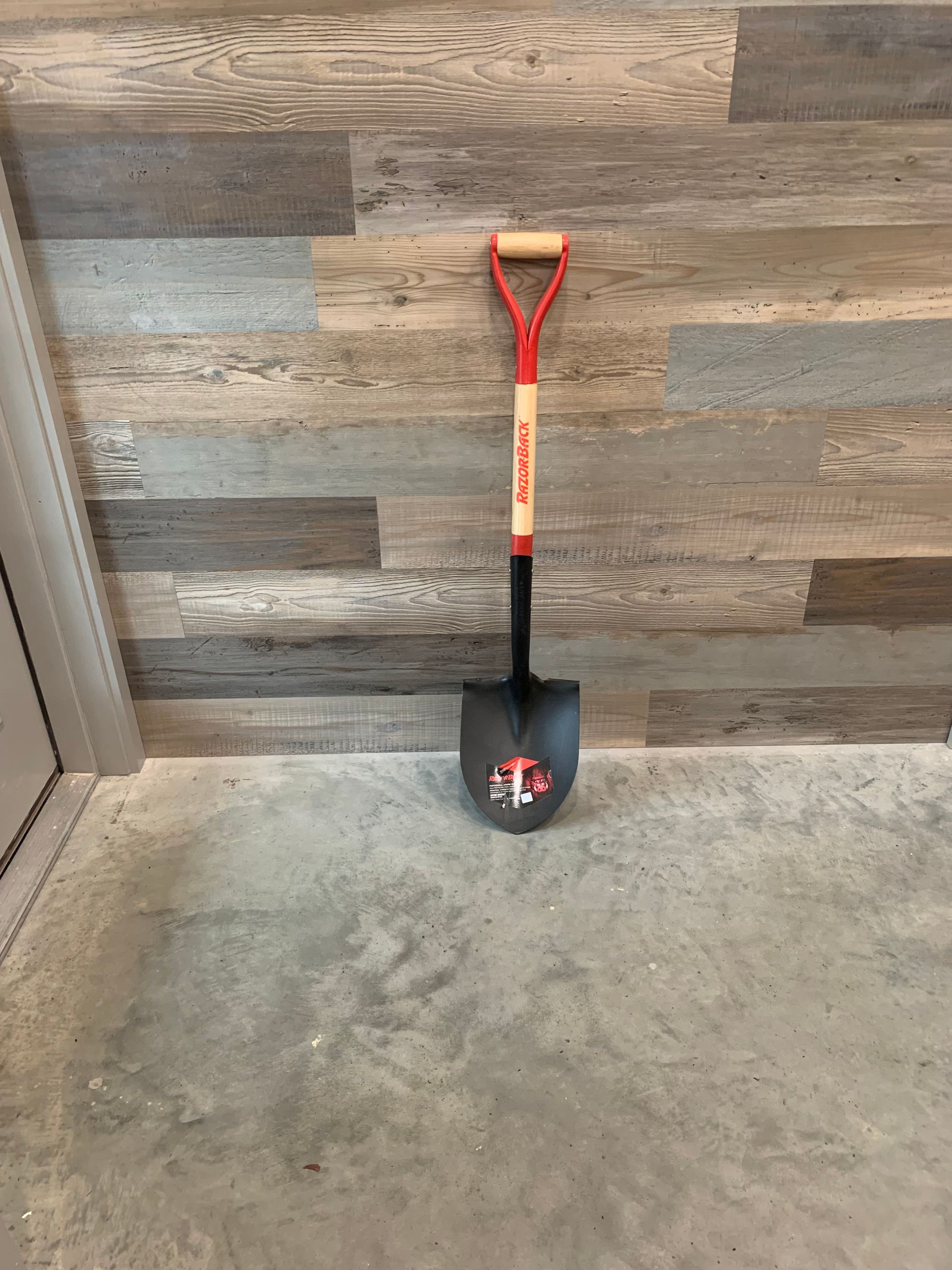 A shovel is sitting on the floor in front of a wooden wall.