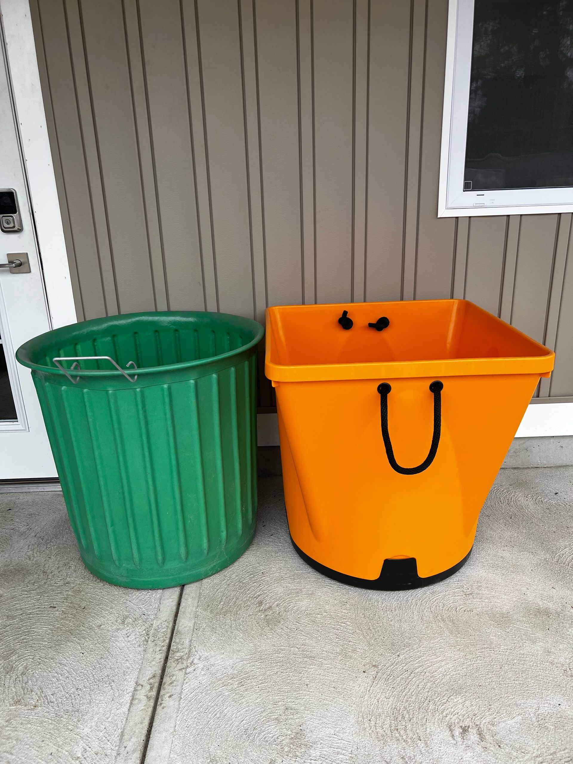 A green trash can and an orange trash can are sitting next to each other
