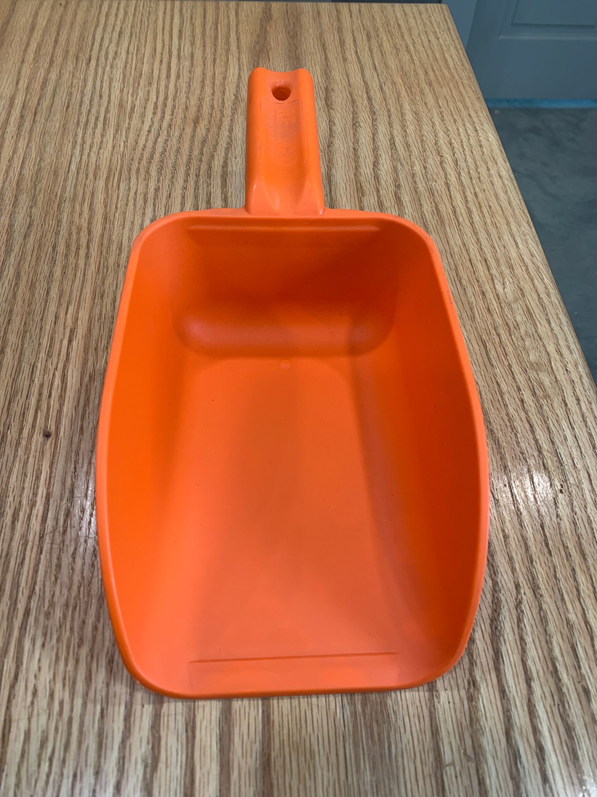 An orange plastic scoop is sitting on a wooden table.