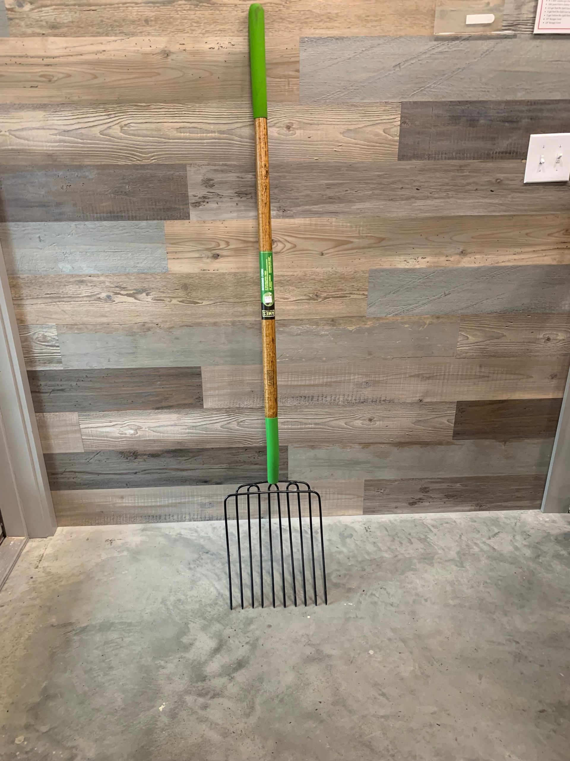 A fork with a green handle is sitting on a concrete floor in front of a wooden wall.