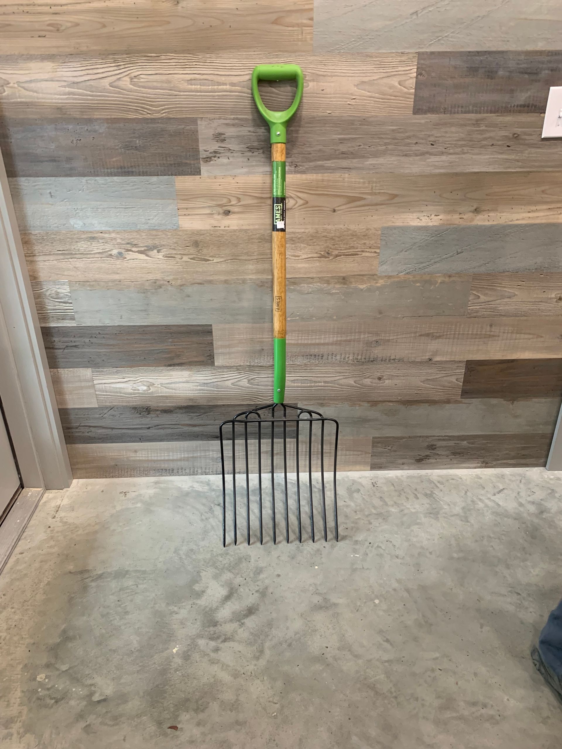 A green fork is sitting on a concrete floor in front of a wooden wall.